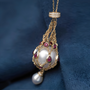 Gold pearl pendant necklace with ruby accents, featuring a large pearl encased in a gold chain cage with a smaller pearl drop
